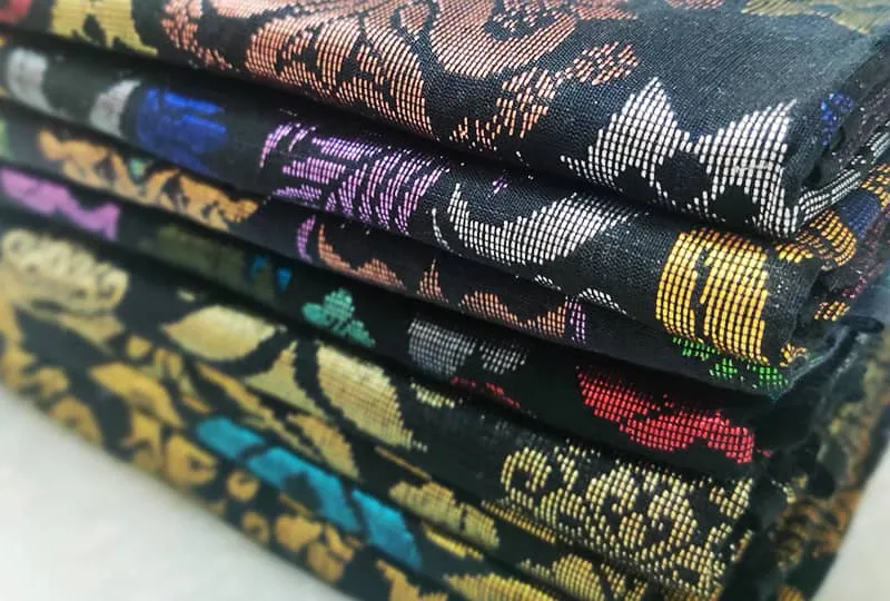 Stack of folded handmade Sampin Songket fabrics in rich floral gold patterns.