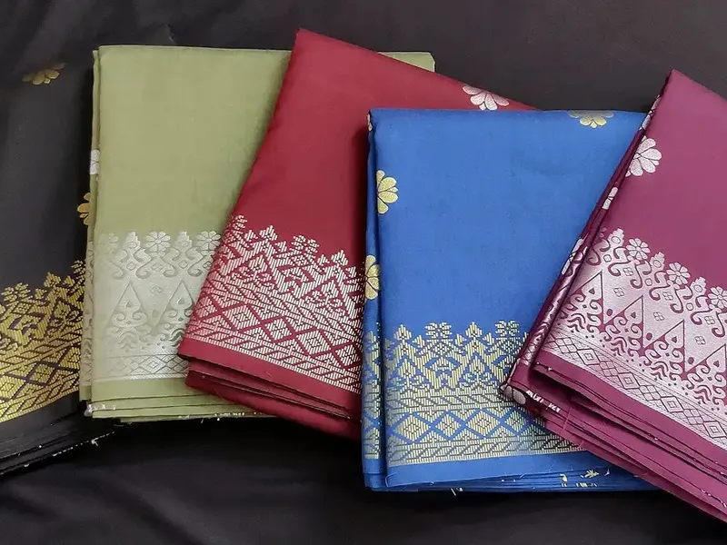 Folded Kain Pasang Songket Tenun fabrics in olive, red and blue with gold woven borders.